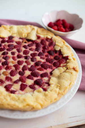 Homemade raspberry cake or galette on white wooden table over a pink cloth, with fresh berries on side, side view, close up, vertical shot.の写真素材
