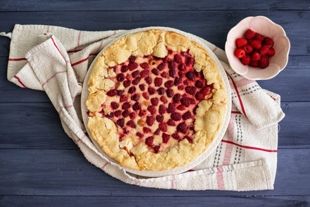 Homemade raspberry cake or galette on blue wooden table over a white cloth, with fresh berries on...