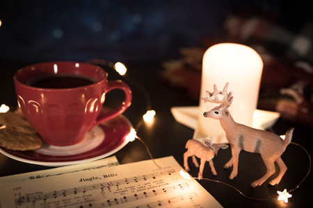 Warm toned Christmas still life with red coffee cup, carol music sheet and deer figurines in candle lit setting.の写真素材