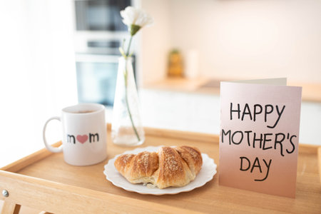 Mother's day still life with mom cup, a sweet pastry and a greeting card on a tray, in airy indoor background.の写真素材