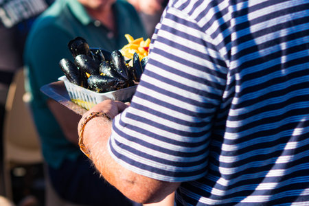 Man with sailor t-shirt taking a mussels portion on a tray at Tregunc Fish Festival, Poissonade 2024.の写真素材