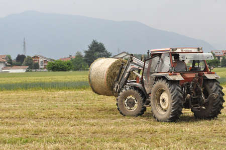 TURIN, ITALY - CIRCA MAY 2020: tractor loading round hay bales made of grass in a fieldのeditorial素材