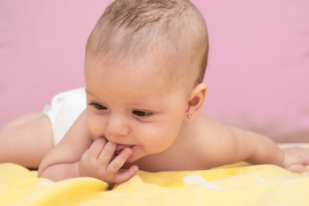 portrait of six month old baby lying with hand on mouth looking to the side