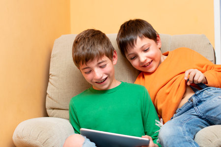 two children laughing with a table in hand on a sofaの写真素材