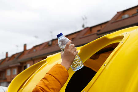 Caucasian boy's hand throwing a clear plastic bottle into a yellow recycling garbage can. Ecological concept, climate changeの写真素材