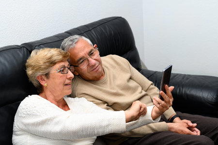 Elderly couple looking at the mobile phone sitting on the sofa at home