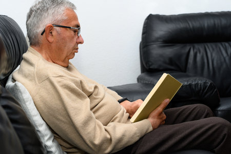 Man with glasses reading a book on the sofa at homeの写真素材