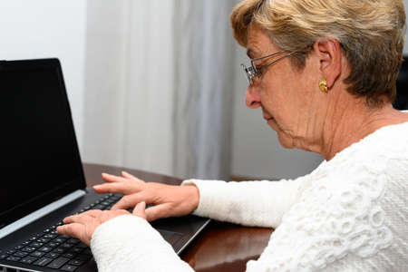 Elderly woman typing on a laptop computer at a table in her homeの写真素材