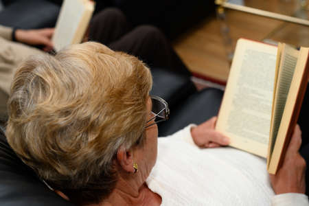 Middle-aged man and woman each reading a book. They are sitting on a sofa in their house.の写真素材