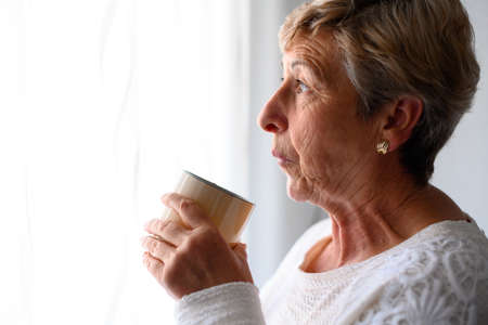 Middle-aged woman looks out the window with cup in handの写真素材