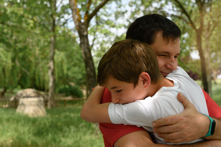 Father and son embrace smiling in a park.