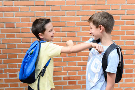 Two smiling children elbow each other. They carry two backpacks, one blue and one black. Concept of back to schoolの写真素材