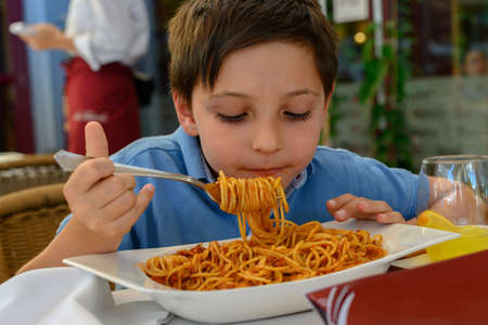 Boy eating spaghetti bolognese at a restaurantの写真素材