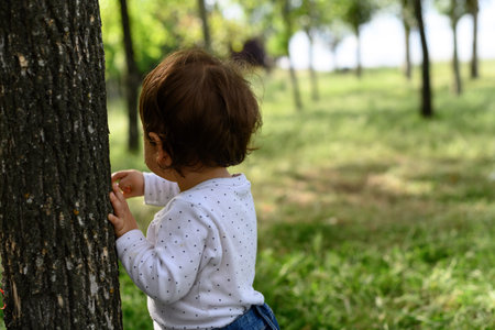Little girl with her back to the trunk of a tree. Trees background with copy space