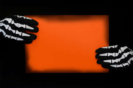 Orange poster held by hands with skeleton gloves. Background for halloween textの写真素材