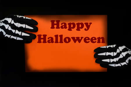 Orange sign held by hands with skeleton gloves. Poster with text saying Happy halloween.の写真素材