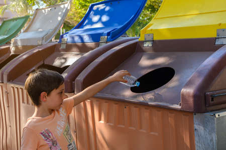 Boy in the street throwing a plastic bottle in the recycling garbage canの写真素材