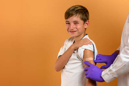 A teenager child smiles as a health worker puts a plaster on his arm. Vaccine conceptの写真素材