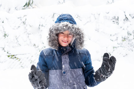 Portrait of a child standing in the snow. The child is wearing winter coat and hood over his head...