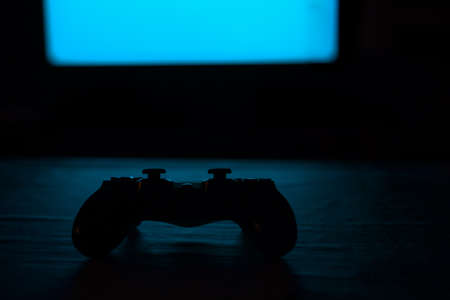 Video game console controller on a table and in front of a blue neon monitor.の写真素材