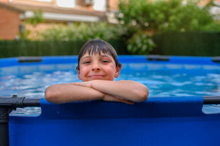 Portrait of smiling child leaning on the edge of a removable swimming pool in the garden of his houseの写真素材
