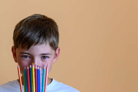 Preteen boy with colored pencils on his face with orange background. Concept of back to schoolの写真素材