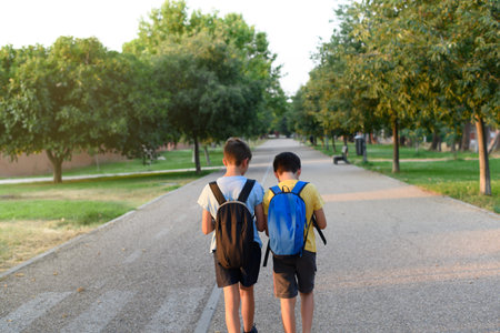 Two children with backpacks on their backs stroll through a park. Concept of back to school