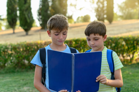 Two student children looking at a blue notebook in the parkの写真素材