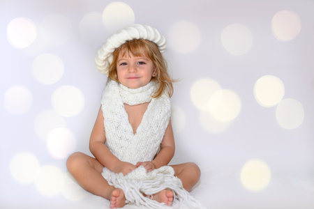 A warm girl wearing a winter beret and a white woolen scarf smiles looking at the camera in a bokeh background.の写真素材
