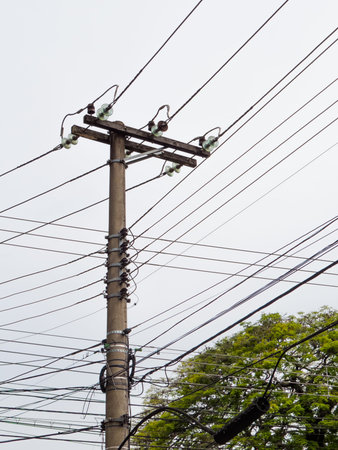 Light pole with electric transmission wires in white background, on a cloudy day