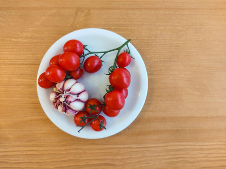 Close up on top view of white plate with bunch of mini tomatoes and garlic on wooden table.の写真素材