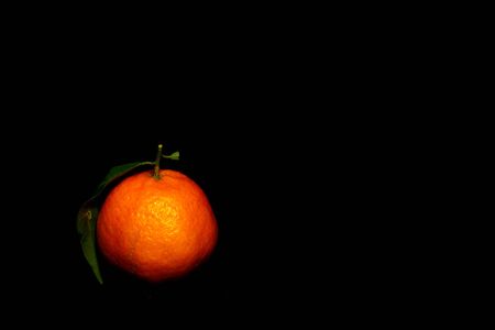 a tangerine on left corner isolated on blackの写真素材