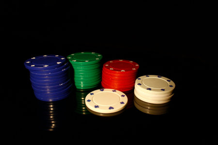 Four colors casino chips stack with a white chip in front, isolated on black with reflection
