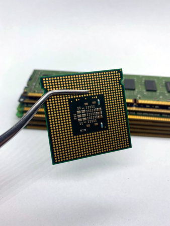 Pincers keeping a microprocessor CPU chip against a stack of RAM close-up isolated on white...