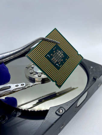 Microprocessor CPU chip on pincer against a silver hard disk plate close-up viewの写真素材