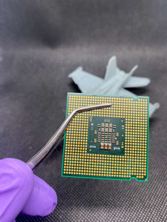 Microprocessor CPU on a pincer and glove hand against an fight plane close-up view with selective focus on foregroundの写真素材