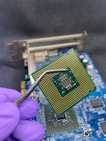 Microprocessor CPU on a pincer and glove hand against a video card close-up view with selective focus on foregroundの写真素材