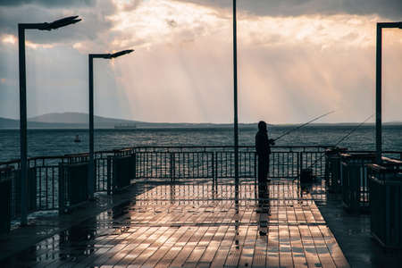 Sunset on a sea bridge after rain in Bulgaria. Reflections on ground. Amazing sea landscape. Fisherman waiting for fish.の写真素材