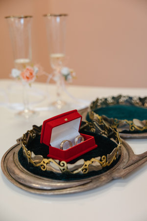Wedding golden rings in a red velvet box in the center of a golden crown. Champagne glasses in the background.の写真素材