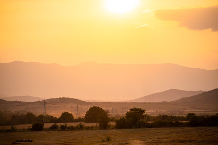 Stunning sunset over the countryside of Bulgaria. Mountain hills in the distance. Beautiful yellow orange skies and trees in the distance.の写真素材
