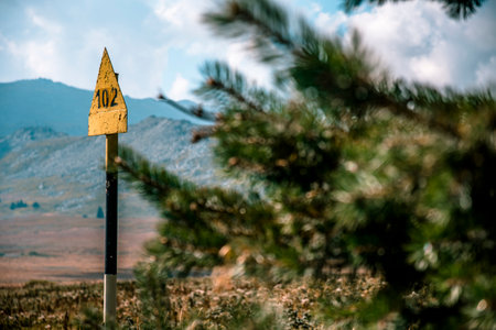 A tree with a mountain in the background. A metal post of a hiking trailの写真素材