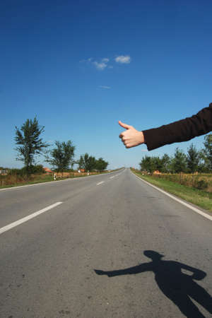 Hitch hike on a road with shadow of hikerの写真素材