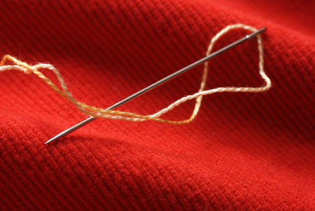 Needle with thread on red background in close up