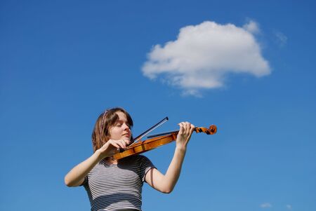 Young girl playing violin over blue sky and cloudの写真素材