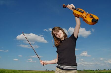 Teenage girl with violin  over blue sky and cloudsの写真素材