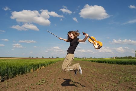 Teenage girl with violin jumping in fieldの写真素材