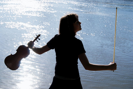 Silhouette of teenage violin player over sunset on river,lake or sea