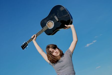 Teenage girl  with black guitar over blue skyの写真素材