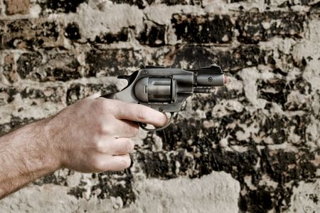 Human hand holding toy gun with brick wall in backgroundの写真素材