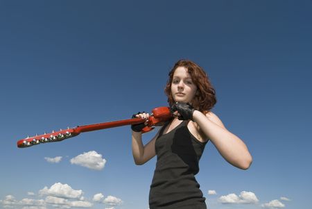Red hair teenage girl with red electric guitar and blue skyの写真素材